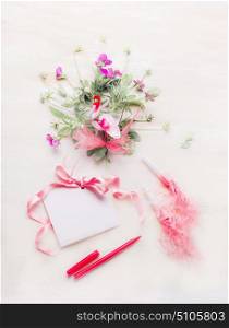 Lovely flowers bunch and blank greeting card with pink ribbon and pen or marker on white wooden background. Festive greeting concept