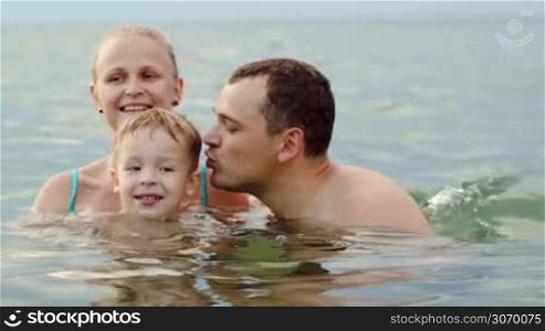 Lovely happy family with little son bathing in sea. Boy and father kissing each other