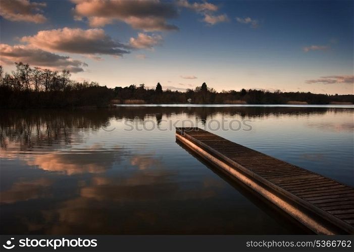 Lovely image of late sunset sky over calm lake landscape with long fishing jetty pier and vibrant colors