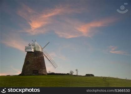 Lovely image of old windmill at sunset on top of hill with vibrant sky