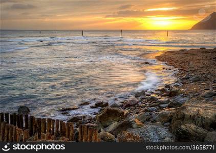 Lovely image of sunrise over incoming tide with rocky foreground and cliffs in background