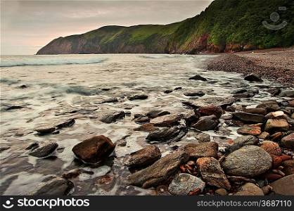 Lovely image of sunrise over incoming tide with rocky foreground and cliffs in background