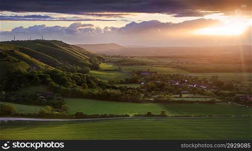Lovely landscape of countryside hills and valleys with setting sun lighting up side of hills whit sun beams through dramatic clouds