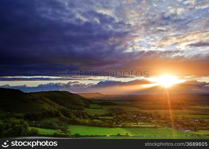 Lovely landscape of countryside hills and valleys with setting sun lighting up side of hills whit sun beams through dramatic clouds