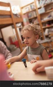 Lovely little boy with curly hair playing with toys standing by the table in the room