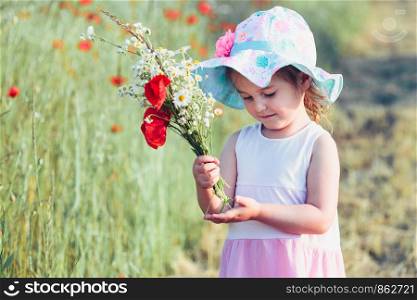 Lovely little girl in the field of wild flowers. Cute girl picking the spring flowers for her mom for Mother's Day in the meadow. Girl holding bouquet of flowers. Spending time close to nature