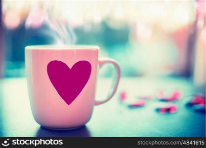 Lovely mug with pink heart on window sill at evening nature background with bokeh, front view. Love symbol or Valentines day concept