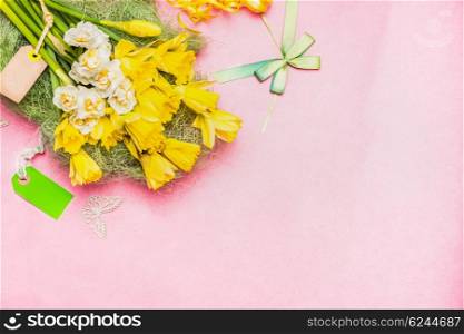 Lovely Narcissus bunch with blank tag and ribbon on pastel pink background, top view, place for text. Festive spring greening card.