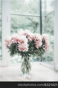 Lovely pastel pink bouquet of peonies in glass vase on floor at window. Flowers in interior design. Cozy home.