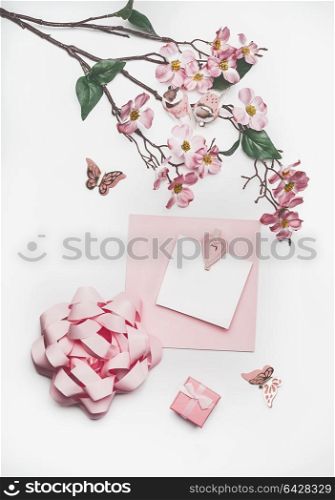 Lovely pastel pink greeting card mock up with blossom decoration, hearts, little gift box and bow on white desk background, top view, flat lay. Wedding invitation layout or Mother Day concept