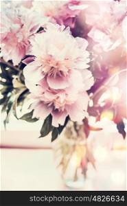 Lovely peonies bunch in glass vase on table with bokeh lighting. Romantic flowers bouquet, front view, pastel color
