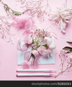 Lovely pink Florist workspace. Beautiful flowers, envelop ,ribbon and markers pencil on pastel background, top view. Creative Invitation and holiday concept