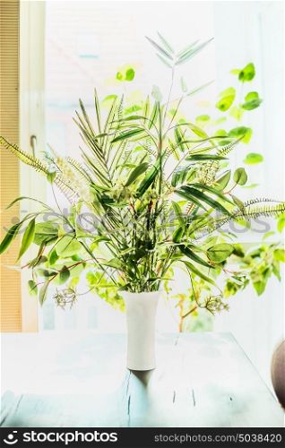 Lovely plants bunch in vase on table at window background. Florist arrangements with variety of green tropical plants.Home decor and interior, backlight