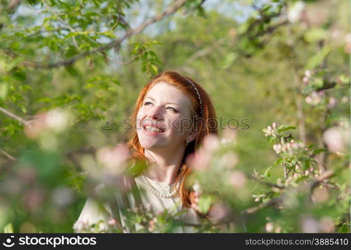 lovely red-haired girl walks in apple orchard