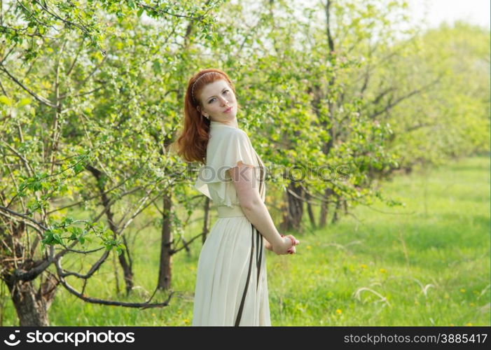 lovely red-haired girl walks in apple orchard