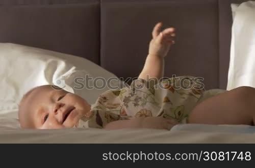 Lovely six months baby girl on bed at home. Active child smiling and touching feet