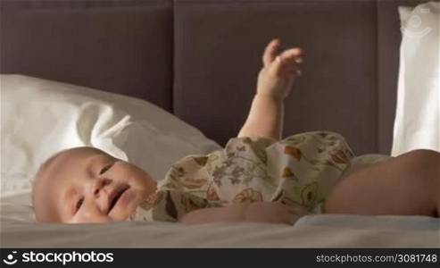 Lovely six months baby girl on bed at home. Active child smiling and touching feet