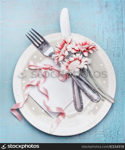 Lovely table place setting in pastel color with plate, cutlery, flowers and card with ribbon on turquoise blue shabby chic background, top view. Mock up for holidays of Mothers day, wedding, Birthday