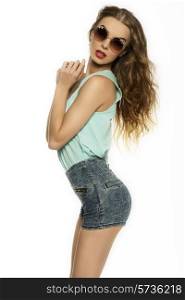 lovely trendy brunette girl posing with sexy denim shorts, blue shirt, long curly hair and vintage sunglasses. Fashion shoot, cute clothes