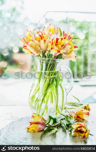 Lovely tulips bunch in glass vase with water on table at spring day background, front view