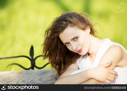 Lovely urban girl in short white dress in the street. Portrait of a happy smiling woman. Fashionable blonde girl sitting on a bench in a city park