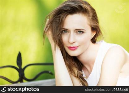 Lovely urban girl sitting on a bench in a city park. Portrait of a happy smiling woman. 