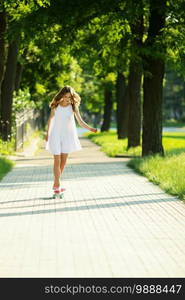 lovely urban woman in white dress with a pink skate. Young girl riding in the park on a skateboard