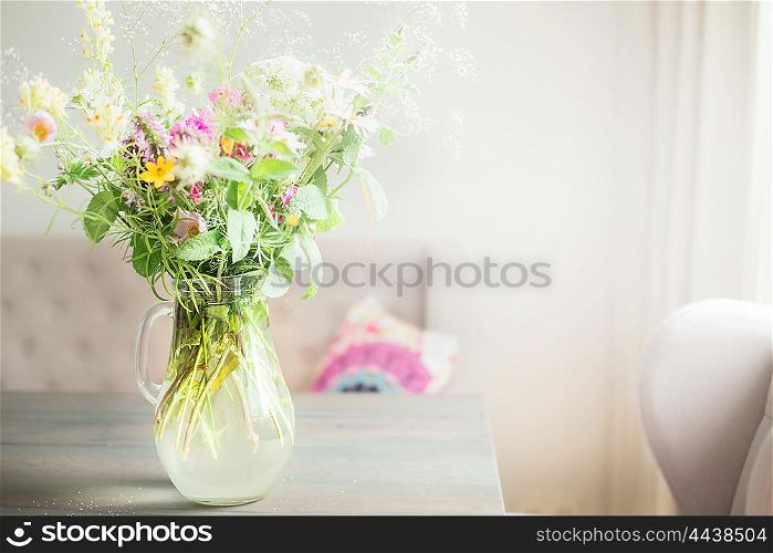 Lovely wild flowers bunch in glass vase on table in light living room , Home decoration and interior.