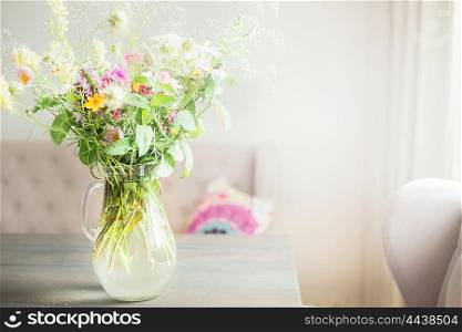 Lovely wild flowers bunch in glass vase on table in light living room , Home decoration and interior.