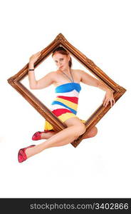 Lovely woman in red blue and yellow striped dress is looking througha picture frame on white background.