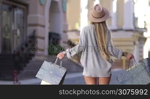 Lovely woman with shopping bags spinning around on city street and smiling. Female brightening with happiness after shopping