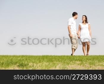 Lovely young couple holding hands and walking on a grass field outdoors