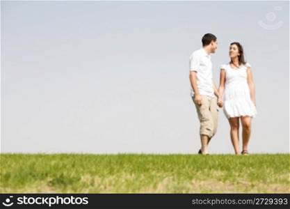 Lovely young couple holding hands and walking on a grass field outdoors