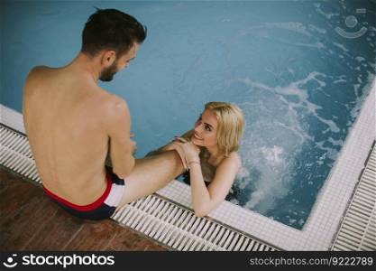 Lovely young couple relaxing on the poolside of interior swimming pool