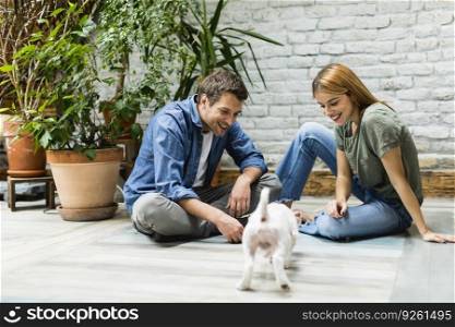 Lovely young couple sitting at rustic living room floor and playing with cute white dog