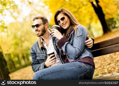 Lovely young couple sitting on the bench with coffee cups in the autumn park
