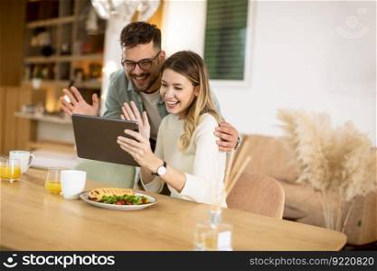 Lovely young couple using digital tablet and having breakfast in the kitchen