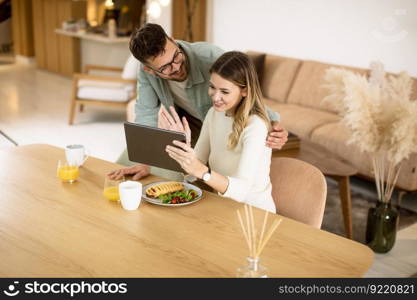 Lovely young couple using digital tablet and having breakfast in the kitchen