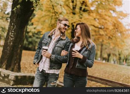 Lovely young couple walking with coffee cups in the autumn park