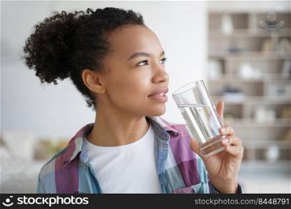 Lovely young hispanic woman enjoying mineral water at home. Positive afro teenage girl drinks water from a glass. Weight loss dieting, fitness and wellness. Healthy lifestyle choice concept.. Lovely young hispanic woman enjoying mineral water. Healthy lifestyle, fitness and wellness.
