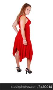 Lovely young woman in high heels standing in the studio in a red dress, long brown hair, and looking over her shoulder. On white background.
