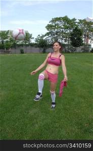 Lovely young woman pracing soccer in a pink shorts and sports braon a soccer field in the sixty.