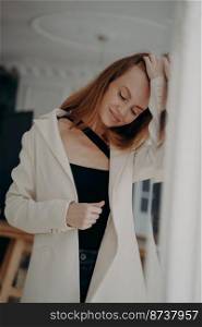 Lovely young woman wearing white suit jacket fixes her hair, posing near mirror. Stylish romantic girl in casual clothing adjusting hairs, going on a date. Female fashion and beauty concept.. Lovely young woman wearing white suit jacket fixes hair posing near mirror. Female fashion, beauty