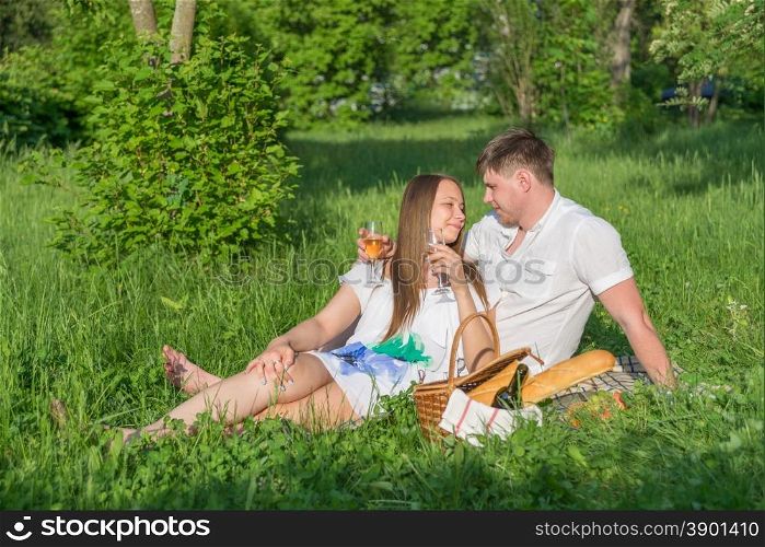 Lovers girl and boy hugging on the grass and looking at each other during a picnic in a city park