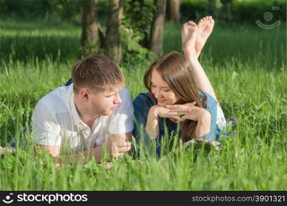 Lovers girl and boy lying on the green grass during a picnic in a city park