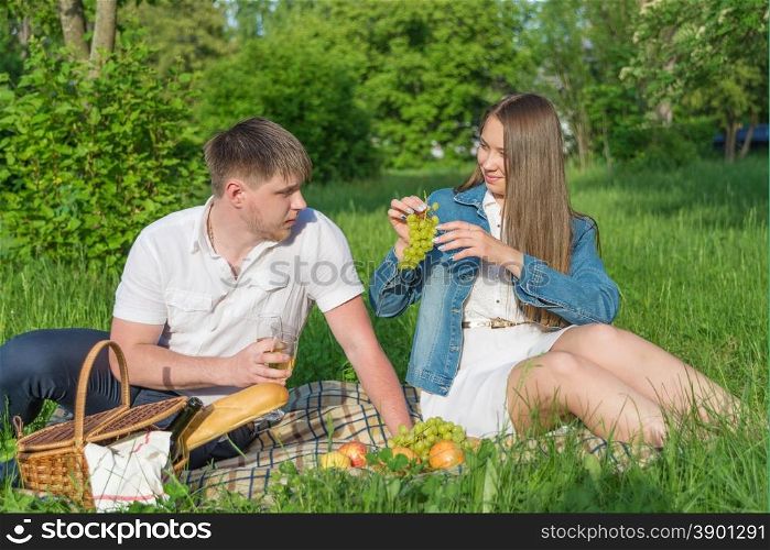 Lovers girl and boy sitting on the grass and eating grapes during a picnic in a city park