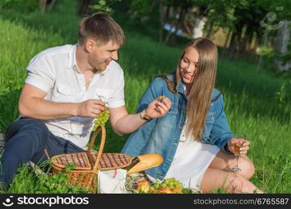 Lovers girl and boy sitting on the grass and eating grapes during a picnic in a city park