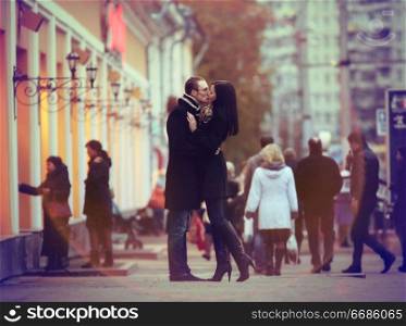 Lovers kissing and cuddling on a city street with passers
