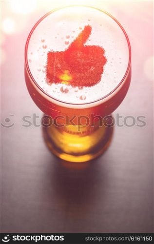 loving beer, thumb symbol on foam in glass on black table, view from above