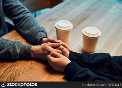 Loving couple holding hands sitting in cafe drinking coffee. Woman and man having a chat, talking together, having a break, relaxing in cafe